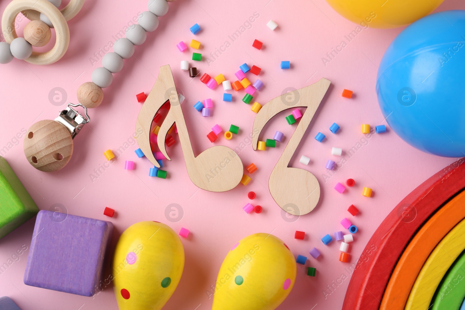 Photo of Baby song concept. Wooden notes, kids maracas and toys on pink background, flat lay