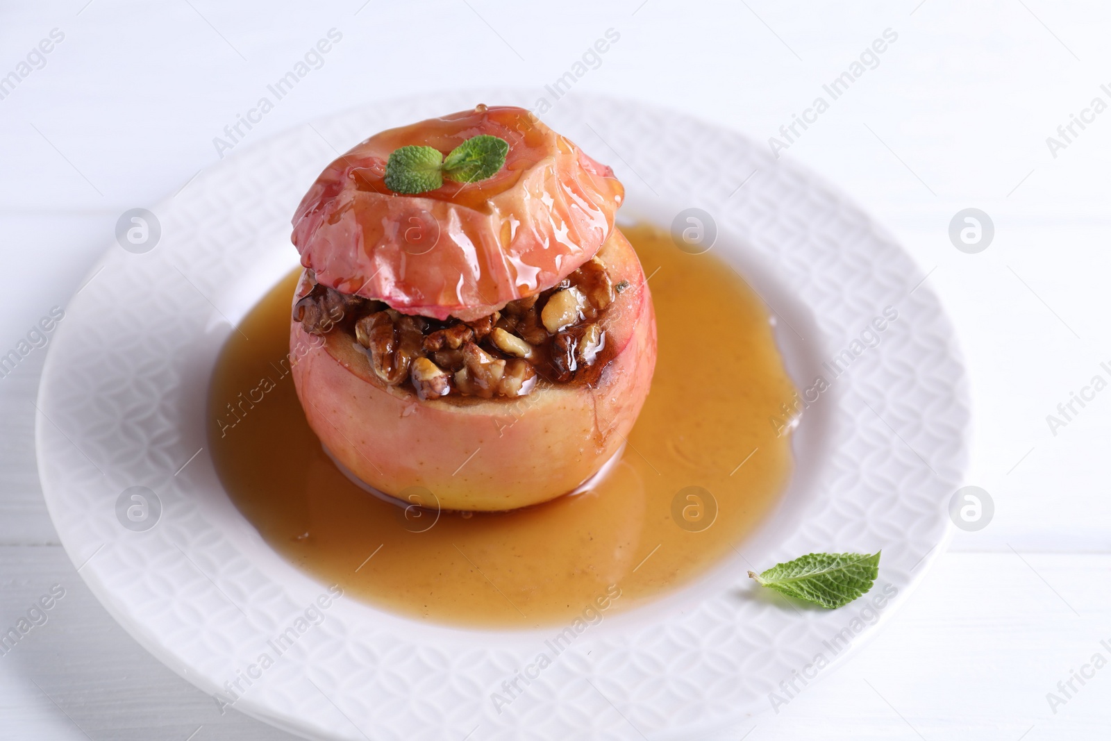 Photo of Tasty baked apple with nuts, honey and mint on white table, closeup