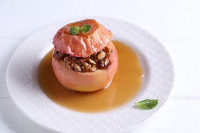 Photo of Tasty baked apple with nuts, honey and mint on white table, closeup