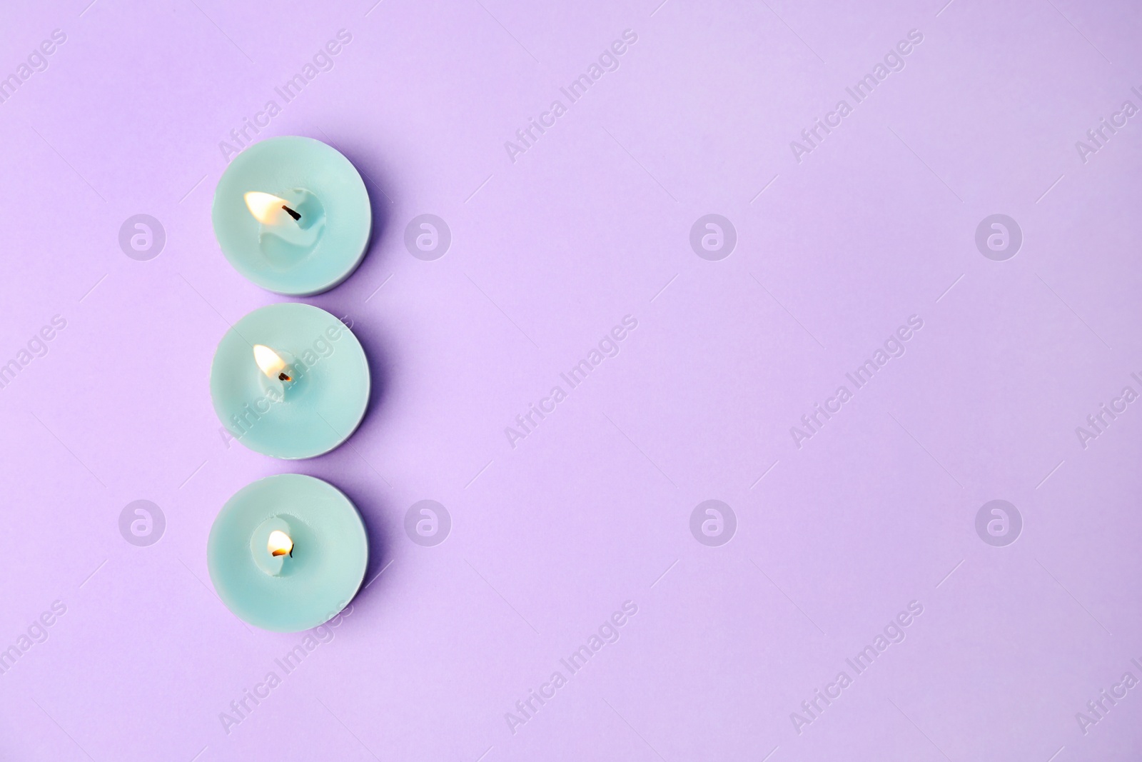 Photo of Burning wax decorative candles on purple background, flat lay. Space for text