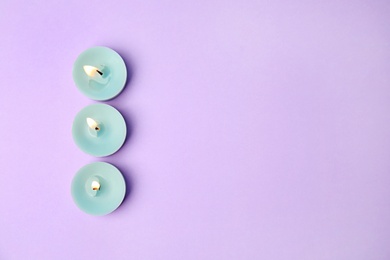 Burning wax decorative candles on purple background, flat lay. Space for text