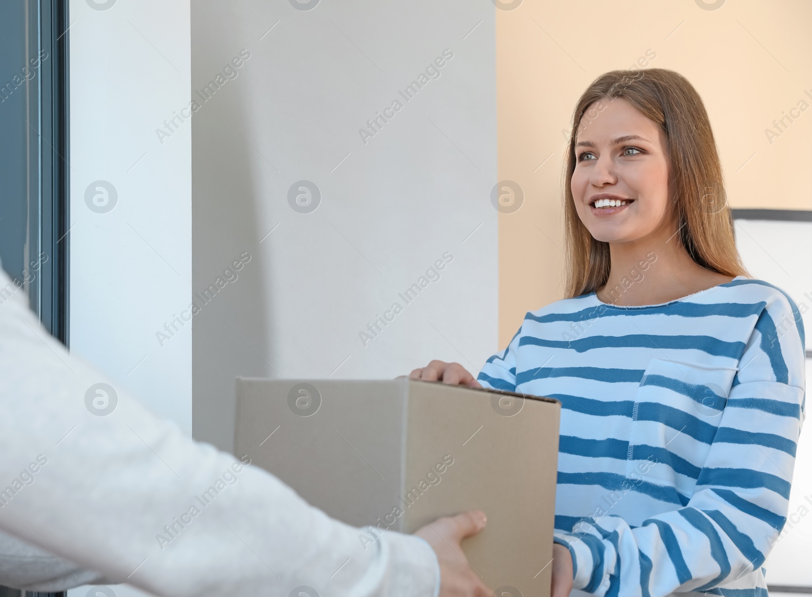 Photo of Woman receiving parcel from delivery service courier indoors