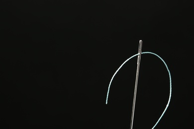 Photo of Needle with sewing thread on black background, closeup