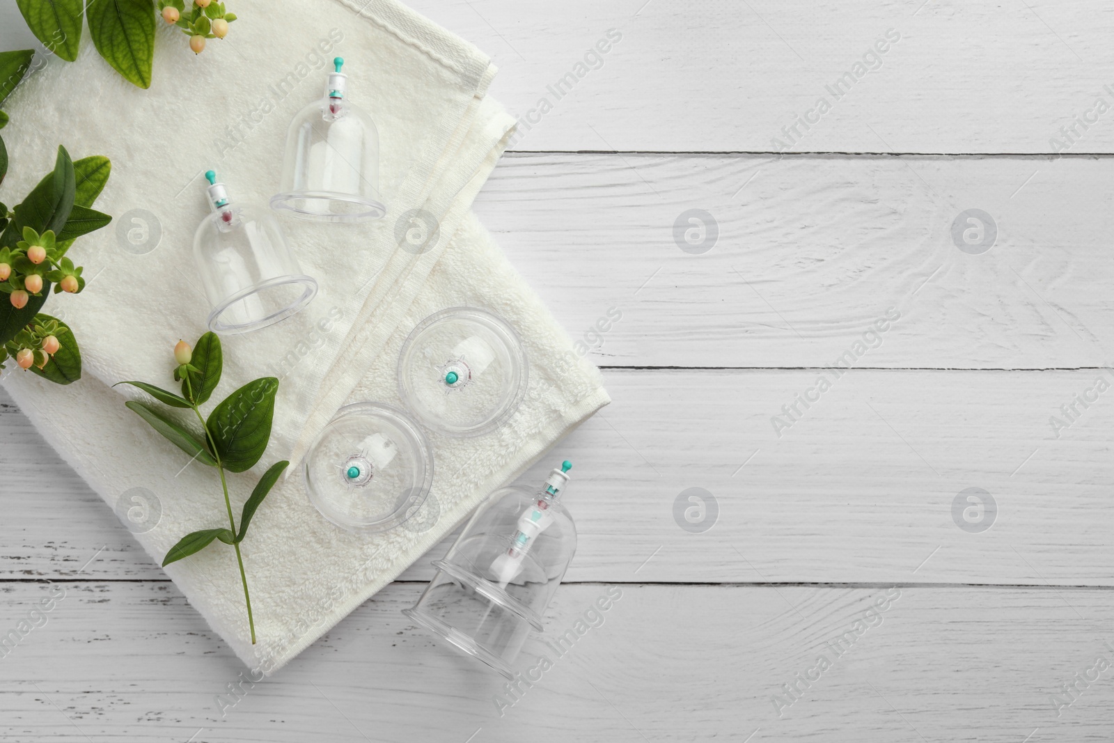 Photo of Cupping therapy. Plastic cups, towels and hypericum perforatum berries on white wooden table, flat lay. Space for text