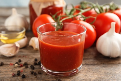 Photo of Composition with glass of tasty tomato sauce on wooden table