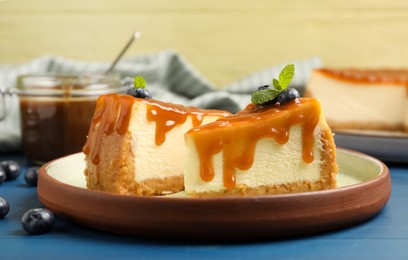 Photo of Pieces of delicious caramel cheesecake with blueberry and mint on blue wooden table, closeup