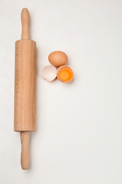 Photo of Raw eggs and rolling pin on white table, flat lay. Baking pie