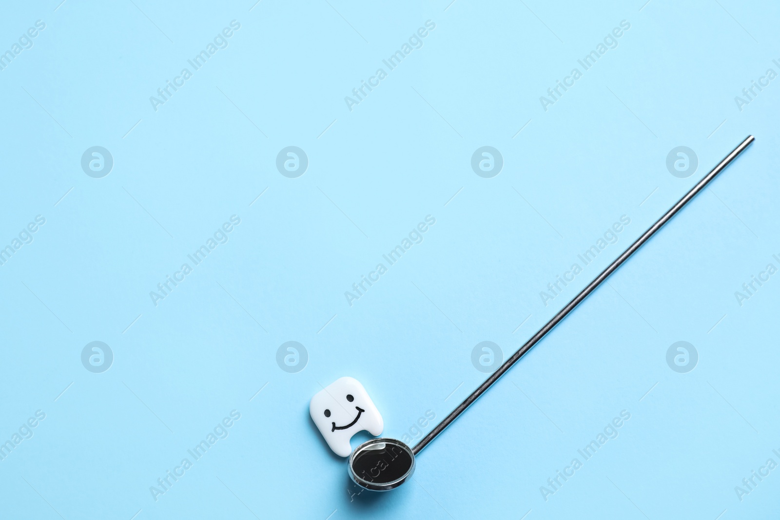 Photo of Professional dental tool and small plastic tooth on light blue background, flat lay