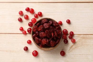 Photo of Dried cranberries in bowl and fresh berries on wooden table, top view