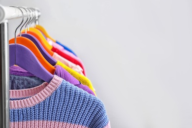 Photo of Colorful clothes hanging on wardrobe rack against light background, closeup. Space for text