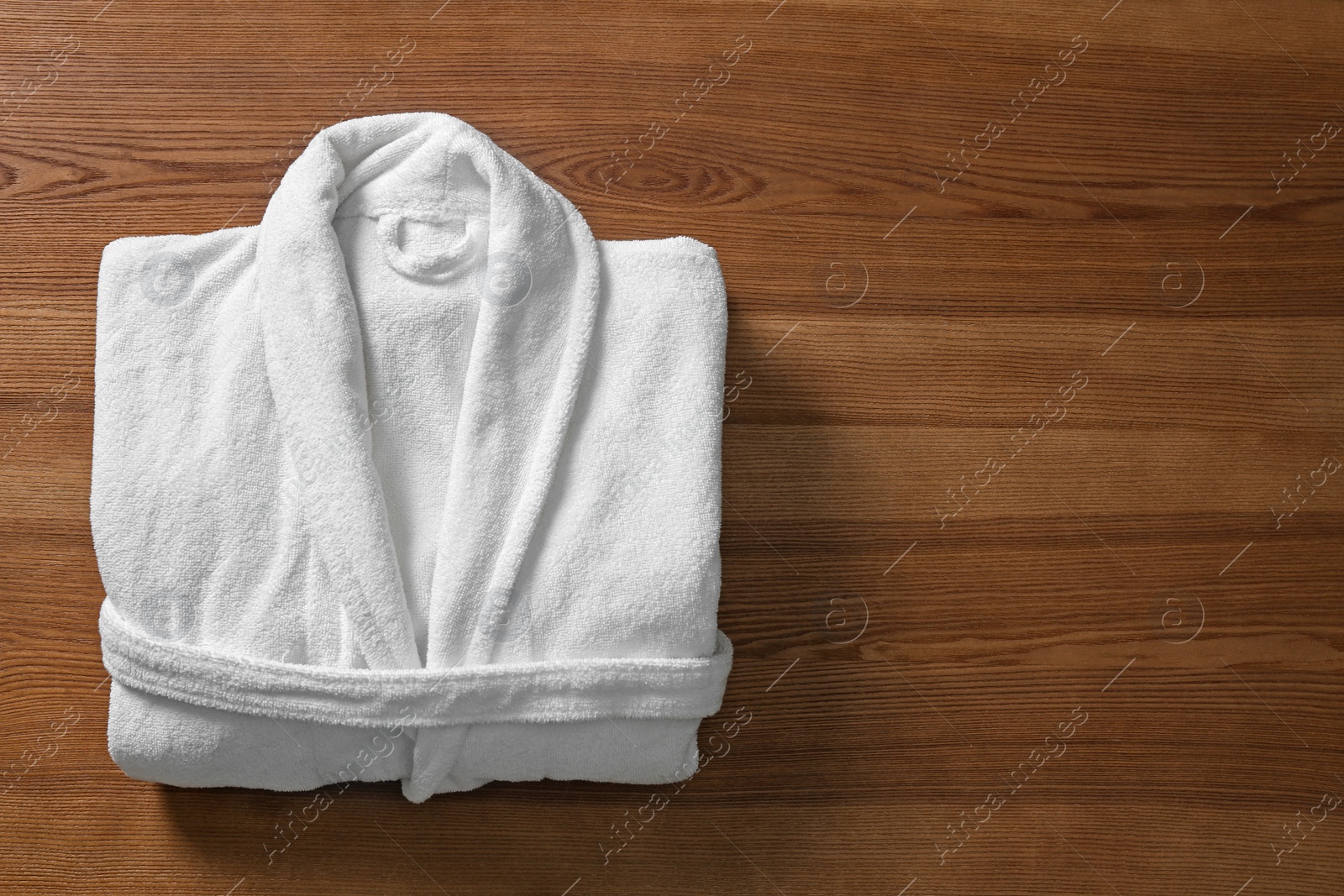 Photo of Clean folded bathrobe on wooden background, top view. Space for text