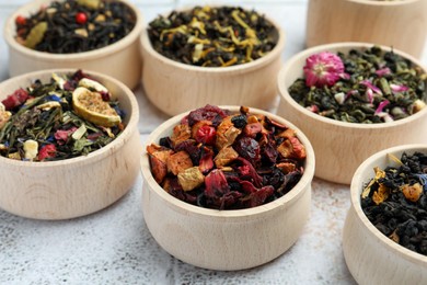 Different kinds of dry herbal tea in wooden bowls on white tiled surface