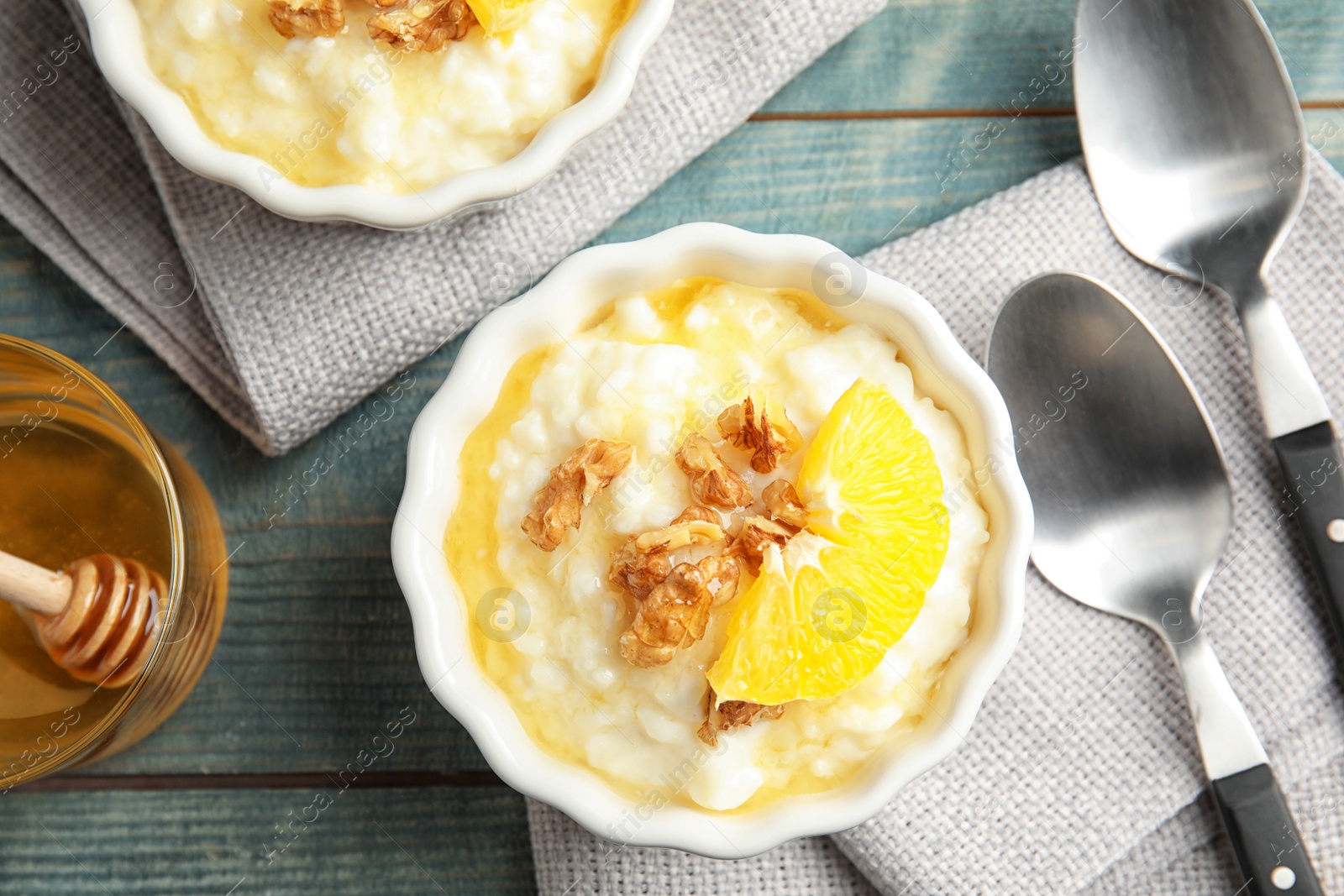 Photo of Creamy rice pudding with walnuts and orange slices in ramekins served on wooden table, top view