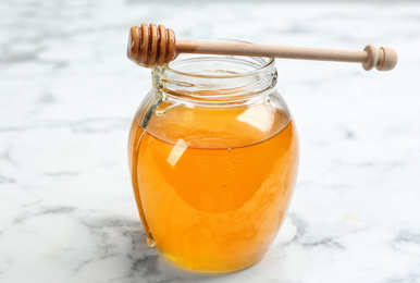 Photo of Tasty honey on white marble table, closeup