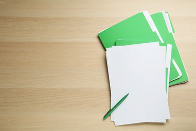 Photo of Light green files with blank sheets of paper and pen on wooden table, flat lay. Space for text