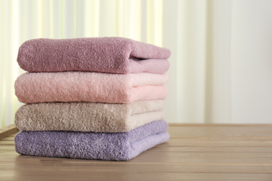 Stack of fresh towels on wooden table in bathroom. Space for text