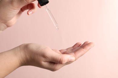 Photo of Woman applying cosmetic serum onto hand on light pink background, closeup