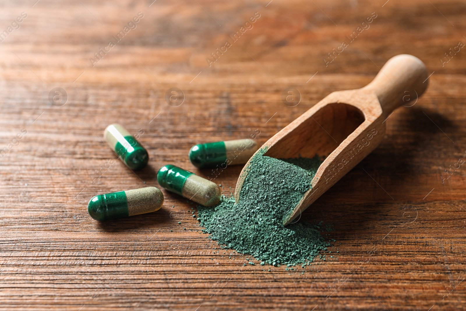 Photo of Scoop of spirulina powder and pills on wooden table