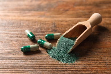 Photo of Scoop of spirulina powder and pills on wooden table