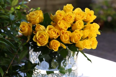 Photo of Beautiful bouquet of yellow roses in glass vase on white table outdoors