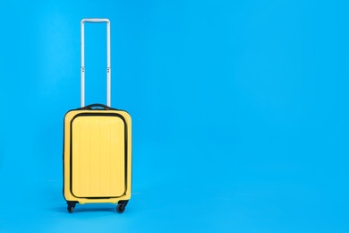 Photo of Yellow travel suitcase on light blue background, space for text. Summer vacation