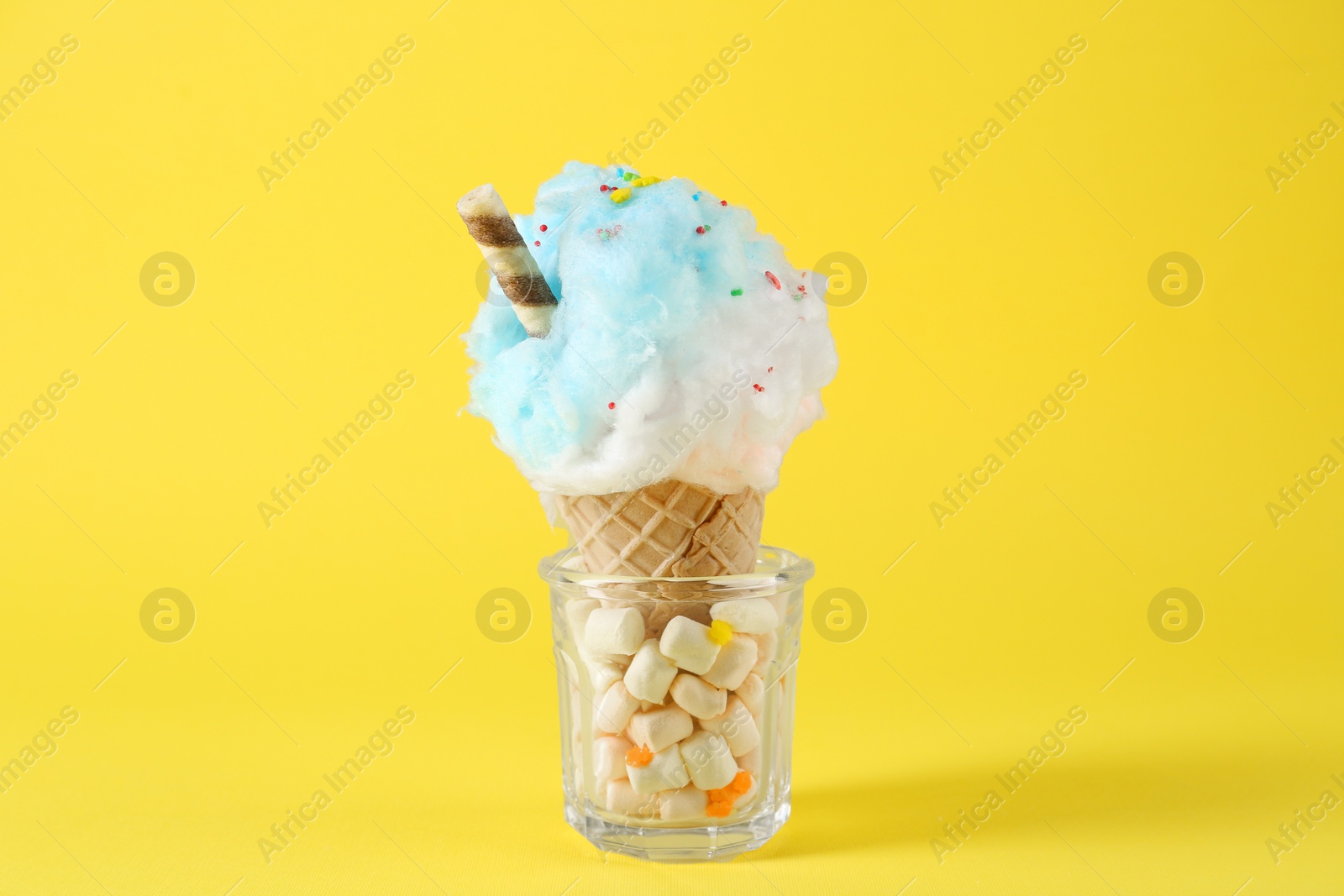 Photo of Sweet cotton candy in waffle cone on yellow background