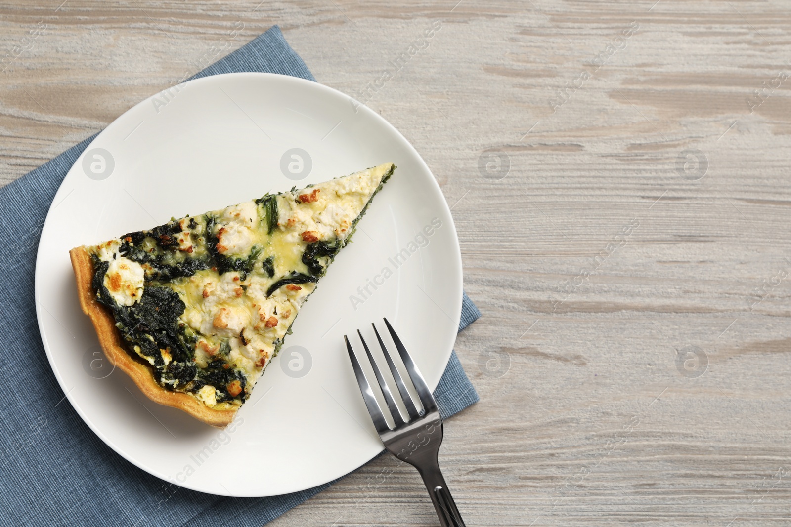 Photo of Piece of delicious homemade spinach quiche on wooden table, top view. Space for text