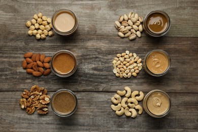Photo of Tasty nut butters in jars and raw nuts on wooden table, flat lay