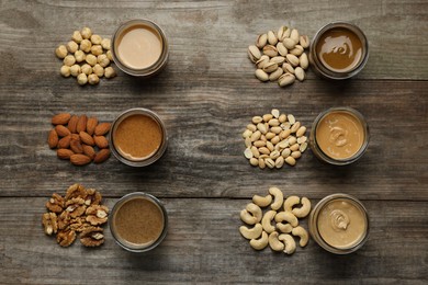 Tasty nut butters in jars and raw nuts on wooden table, flat lay