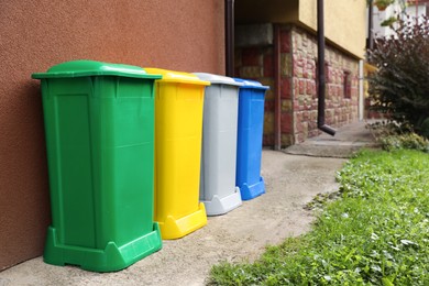 Many colorful recycling bins near brown wall outdoors