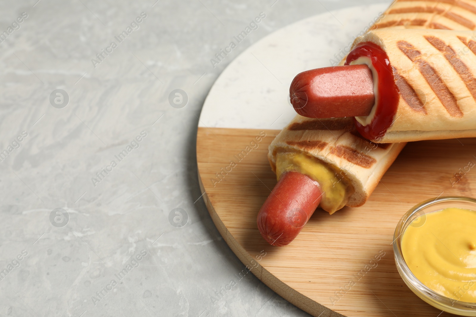 Photo of Tasty french hot dogs and dip sauce on light grey marble table, space for text