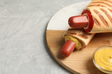 Tasty french hot dogs and dip sauce on light grey marble table, space for text