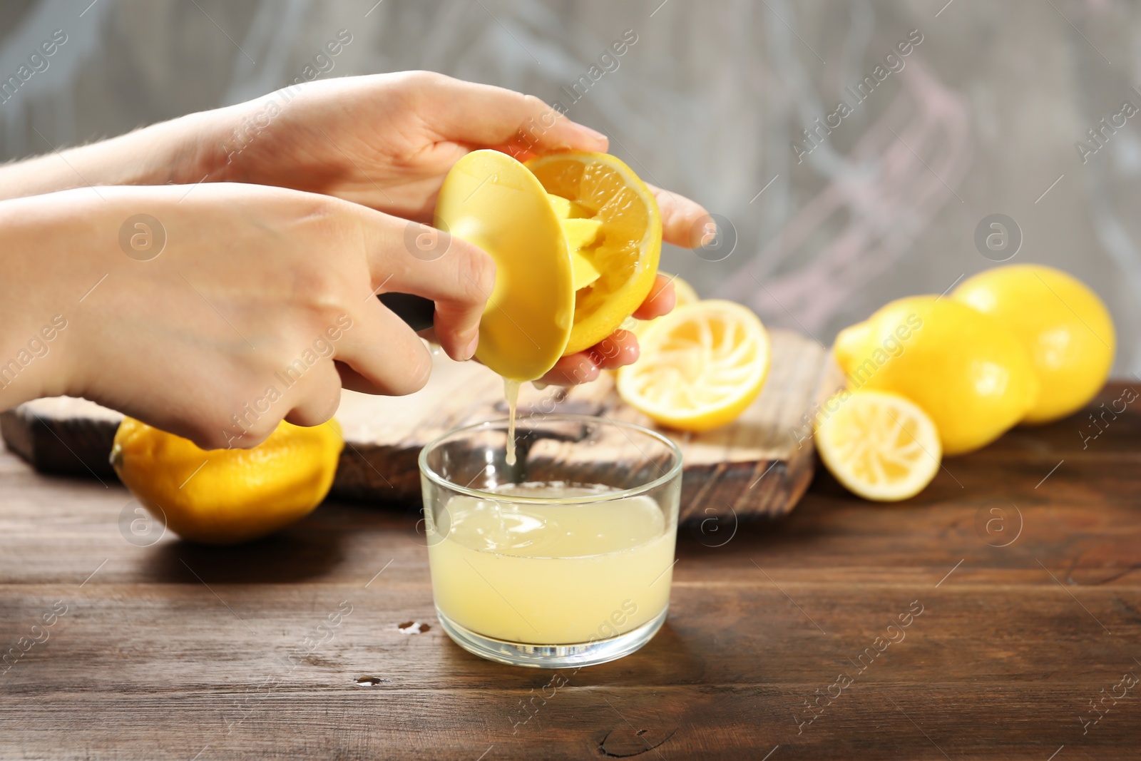 Photo of Young woman squeezing lemon juice with reamer into glass on table