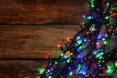 Photo of Glowing festive lights on wooden table, top view. Space for text