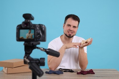 Smiling fashion blogger showing bow ties while recording video at table against light blue background