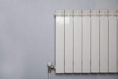 Photo of Modern heating radiator on light wall indoors, space for text