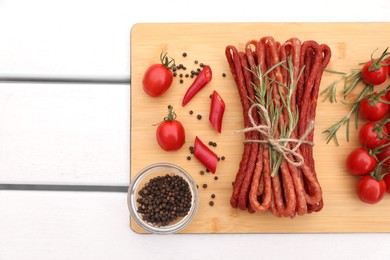 Photo of Bundle of delicious kabanosy with pepper, tomatoes and rosemary on white wooden table, top view. Space for text