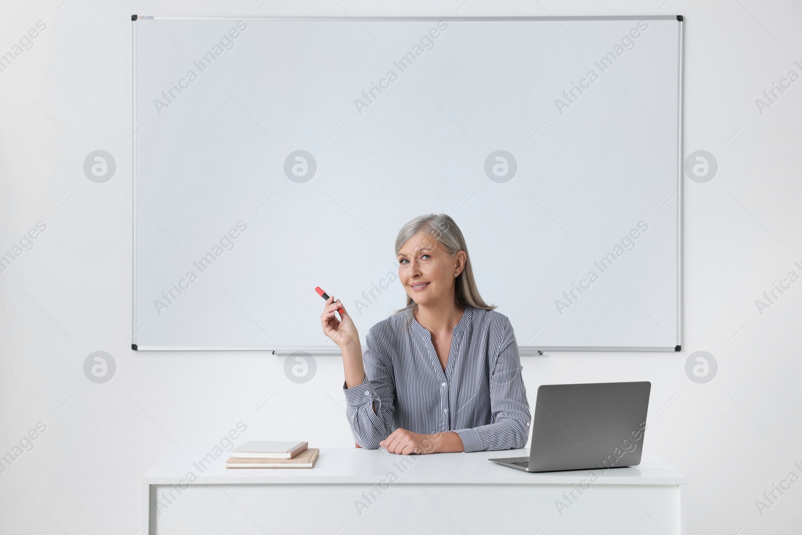 Photo of Happy professor giving lecture near laptop at desk in classroom