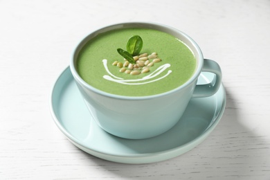 Photo of Cup of healthy green soup with fresh spinach on white wooden table