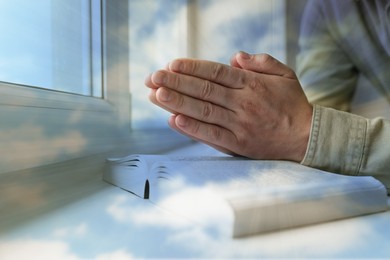 Image of Religion. Double exposure of sky and Christian man praying over Bible at windowsill, closeup