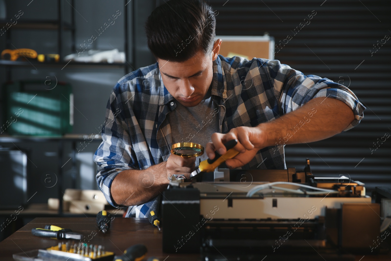 Photo of Repairman with magnifying glass and pliers fixing modern printer in office