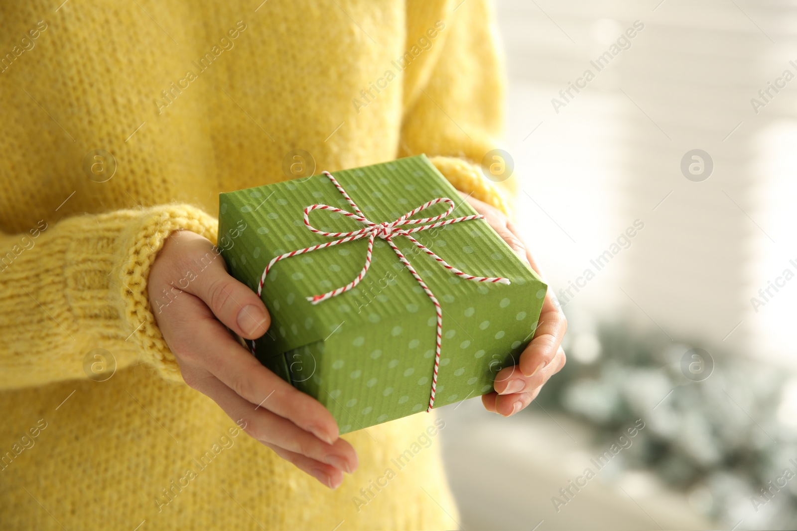 Photo of Woman holding green Christmas gift box indoors, closeup