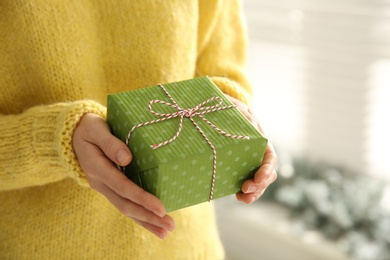 Woman holding green Christmas gift box indoors, closeup