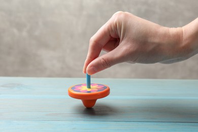 Woman playing with bright spinning top at light blue wooden table, closeup