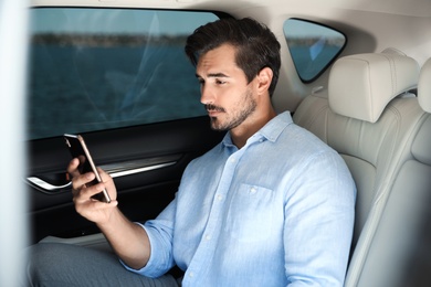 Photo of Attractive young man with smartphone on backseat in luxury car