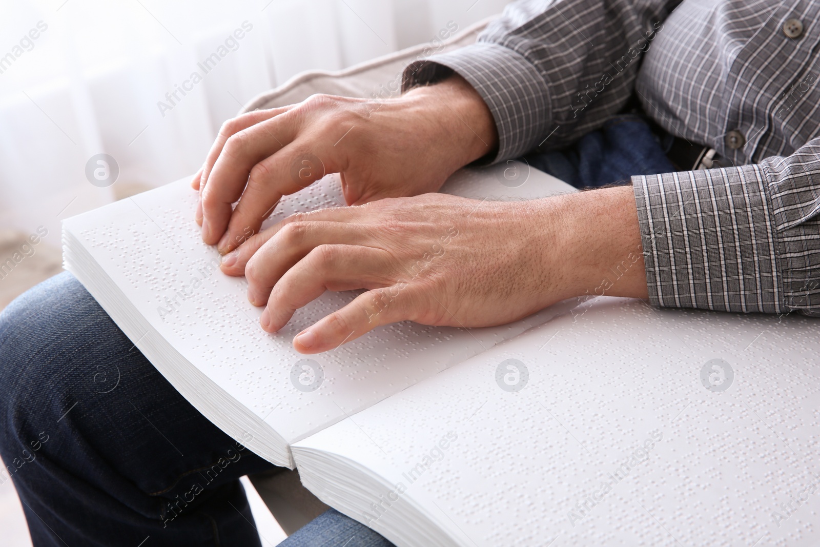 Photo of Blind man reading book written in Braille at home, closeup
