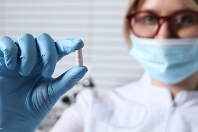 Photo of Doctor holding pill on light background, selective focus. Space for text