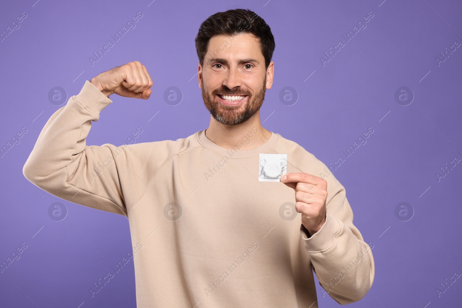 Photo of Happy man holding condom on purple background. Safe sex