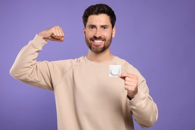 Happy man holding condom on purple background. Safe sex