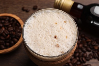 Bottle of delicious syrup, glass of coffee and beans on wooden table, closeup